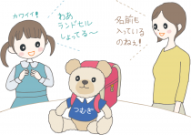 イラスト:ランドセルを背負った名入れのぬいぐるみをもらって大喜びの新入学女子と「名前も入っているのねぇ」と感心するお母さん