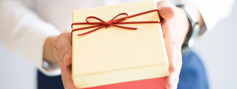 Closeup of person giving big gift box with bow. Man greeting someone. Gift concept. Isolated cropped view on grey background.